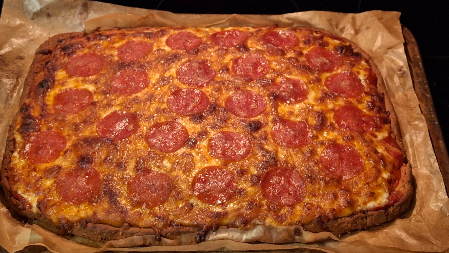 Homemade rectangular pepperoni pizza with melted golden cheese, tomato sauce, and pepperoni baked on a pizza stone.
